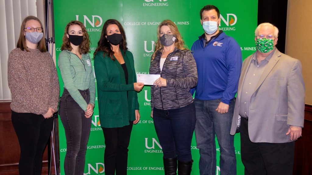 Senior ChE students Charlie Lien and Lindsay Molina assist Robin Turner, UND Alumni Foundation Director of Development in accepting the donation from Tammy Moe, Factory Cost Accountant and Keaton Hanevold, Engineering Superintendent, BSChE 2016. Course instructor Wayne Seames stands next to Mr. Hanevold.