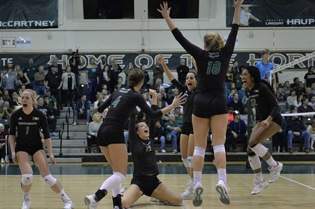 UND Volleyball's Faith Dooley (kneeling) is joined by teammates celebrating the match point that catapulted them to a second-straight Big Sky Conference  Championship and berth in the NCAA National Tournament.  The Fighting Hawks defeated host team Sacramento State 3-2 in a grueling roller-coaster match. Image courtesy of Sacramento State Athletics.
