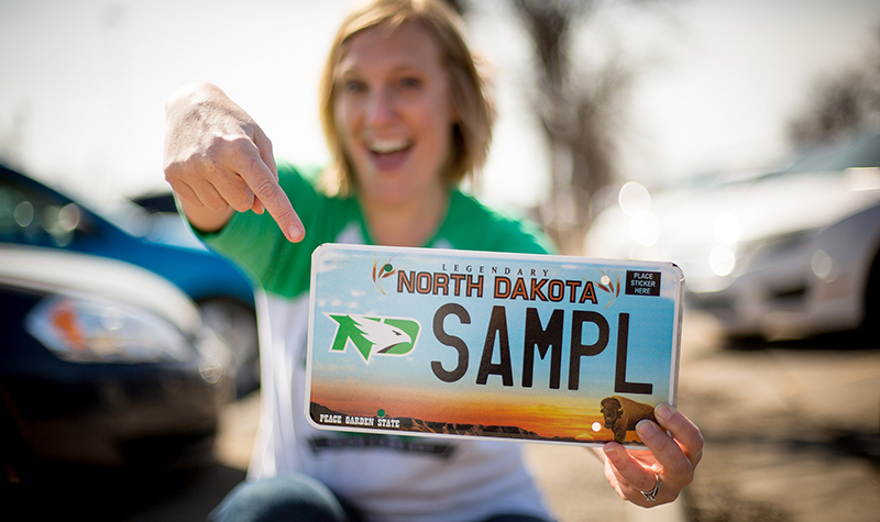 Alyssa Konickson, UND Alumni Association & Foundation director of communications, shows off an example of one of the new North Dakota license plates , marked with the Fighting Hawks logo. Image courtesy of Sam Melquist, AA&F.
