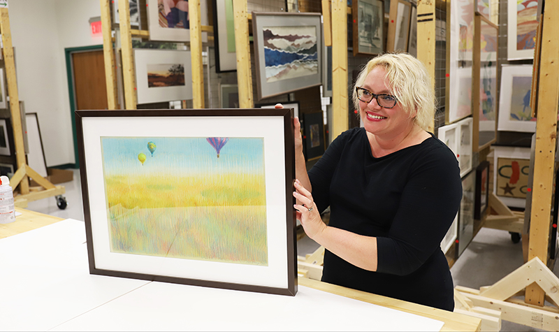 UND Art Collections Manager and Curator Sarah Heitkamp holds Balloon Shadows, a pastel piece created by Jackie McElroy-Edwards in 1982. The piece is one of 25 uniquely framed by Heitkamp’s Art Collections team for an upcoming exhibit of McElroy-Edwards’ work. Photo by Connor Murphy/UND Today.
