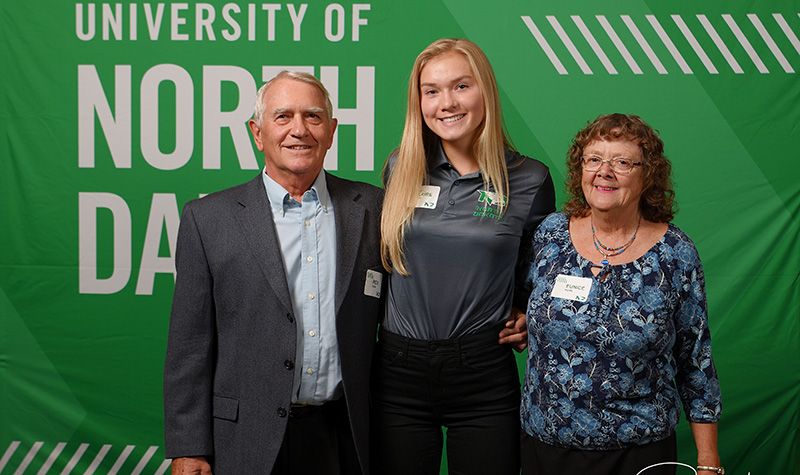 Pete and Eunice Kuhn pose for a photo with UND women's basketball freshman Claire Orth (middle). Over the years, the Kuhns have donated to countless areas, including scholarships for Fighting Hawks Athletics, the College of Business & Public Administration, and the College of Education & Human Development; as well as the building of the Betty Englestad Sioux Center and the High Performance Center; a media center for basketball and locker rooms for football and volleyball. Image courtesy of the UND Alumni Association & Foundation, and Russ Hons Photography.