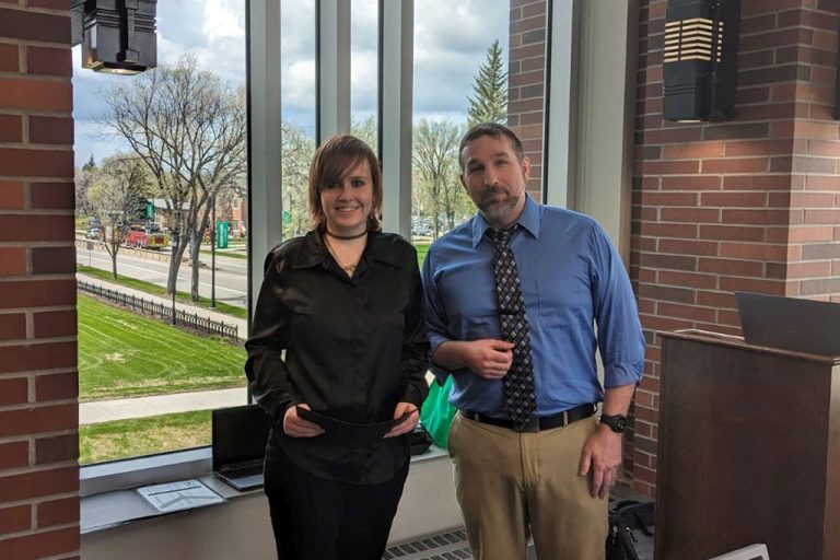 Professor and student stand in front of window