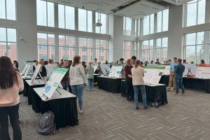 students giving poster presentations in ballroom with high windows
