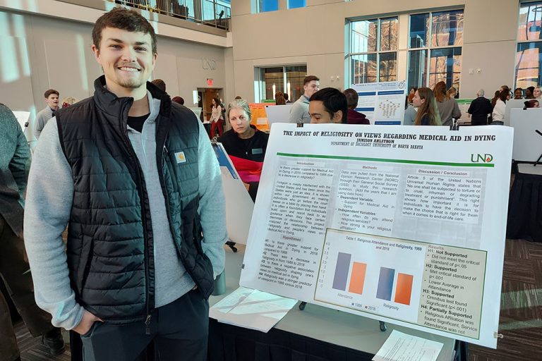 male student stands next to research poster