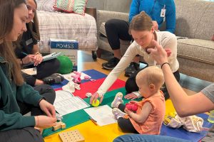 college students interact with toddler with toys