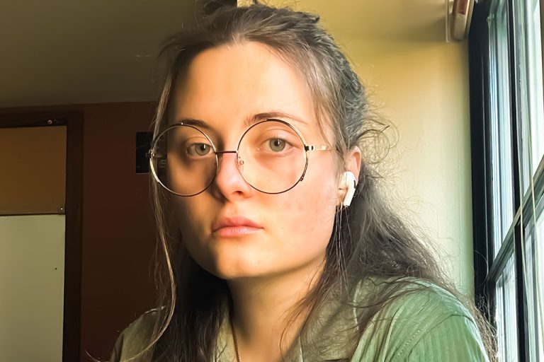 person with round glasses standing near window