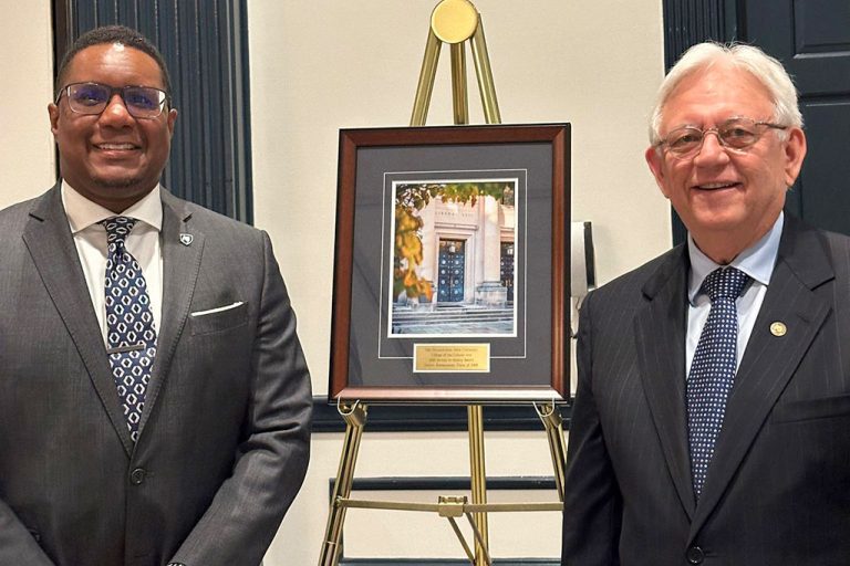 Two men stand in front of a plaque on a stand