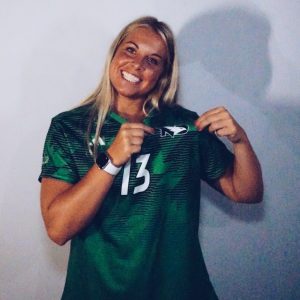 CSD student-athlete Katie Alto in Fighting Hawks uniform celebrating team logo against blank wall