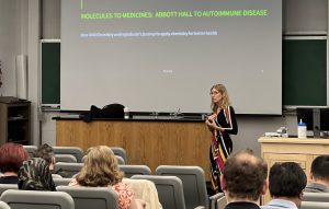 Dr. Stacie Bell at the front of a lecture room, speaking to filled seats