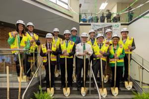 Group in lobby of Upson Hall for ceremonial ground breaking. All in high-visibility vests and white hard hats, posing with golden shovels.