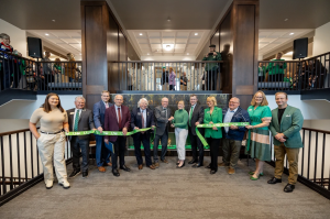 Group of individuals holding green UND ribbon and giant scissors in front of new Merrifield Fireplace Lobby