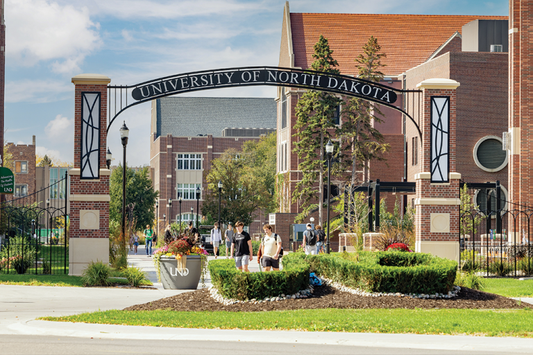 University of North Dakota archway with crisp landscaping and students walking under a wispy blue sky.