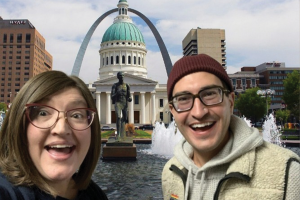 Dr. Legerski and Dr. Bartholomay smiling in a selfie photo in front of the St. Louis Arch and capitol building with fountains.