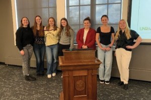 Seven sociology students lined up for a photo side by side, behind wooden UND podium in a Chester Fritz Library meeting room.