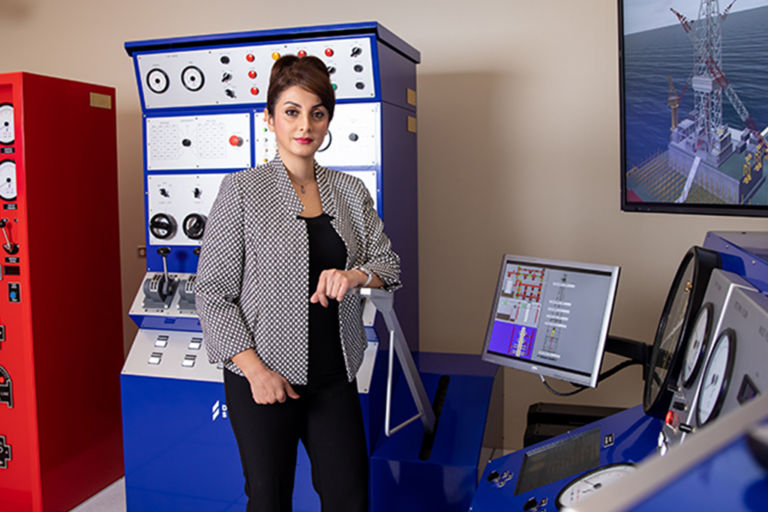 A professor poses with an impressive drilling simulator, complete with detailed digital displays and immersive equipment.