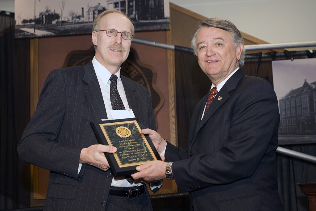 Mike Mann (left), who recently retired after a 41-year teaching and research career at UND, receives the UND Foundation/Thomas J. Clifford Faculty Achievement Award for Excellence in Research from former UND President Charles Kupchella on Founders Day in 2006. UND archival photo.