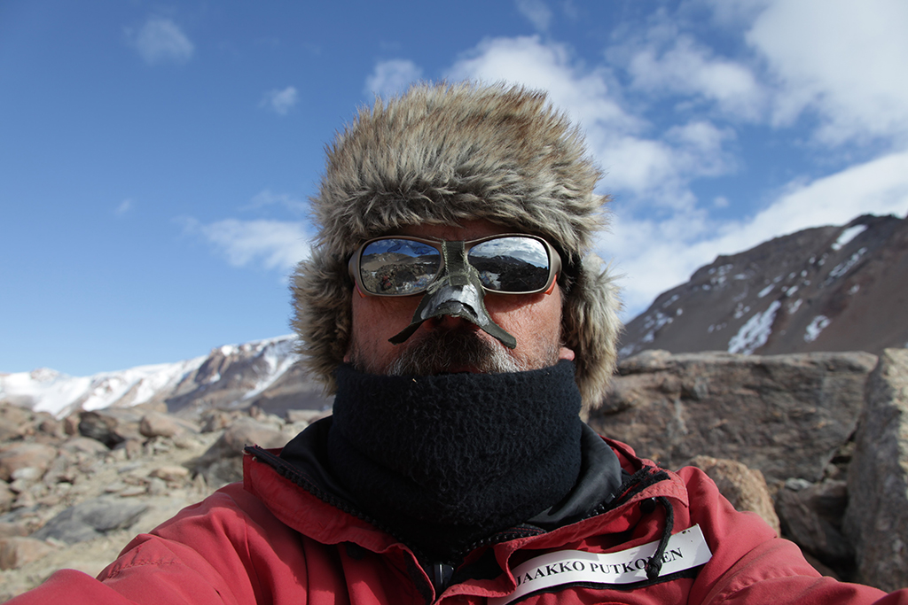 Person wearing winter gear, sunglasses, and a protective nose piece.
