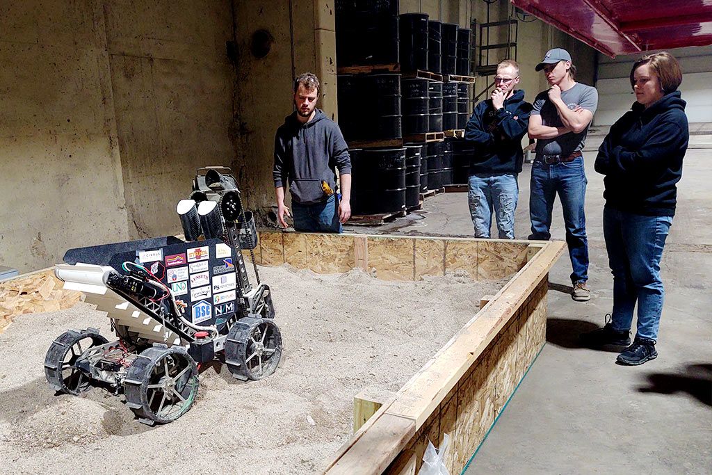 Team members look at their lunar excavation robot functioning inside a simulated environment