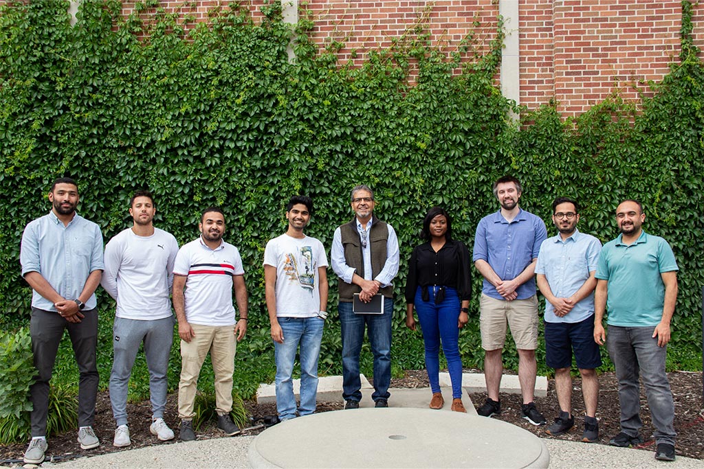 Research group members stand outside against an ivy-clad wall on campus