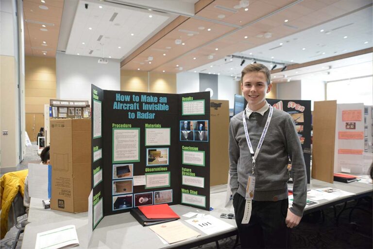 Student stands proudly next to science fair project