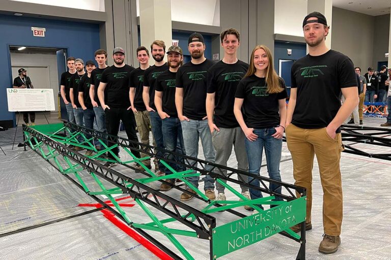 Students stand proudly next to model bridge construction
