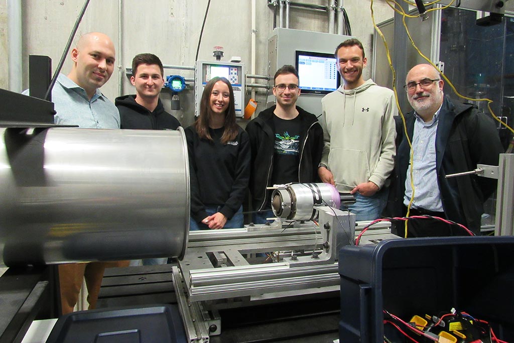 People stand around laboratory equipment and a small turbine engine rocket.
