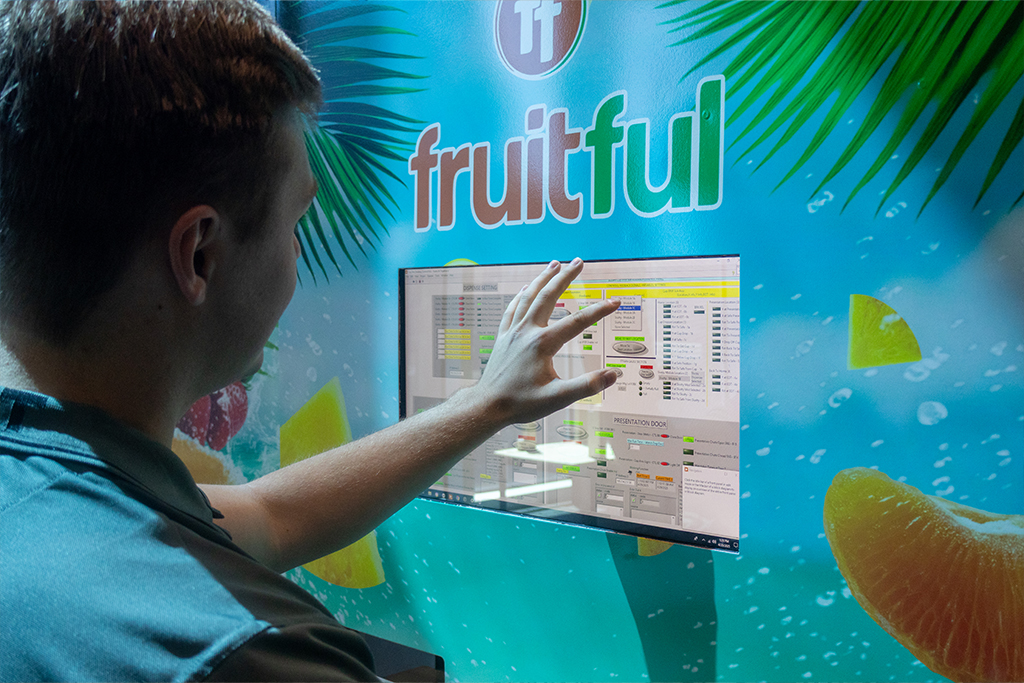 A student presses a button on a vibrant display that is located on the front of a brightly colored vending machine.