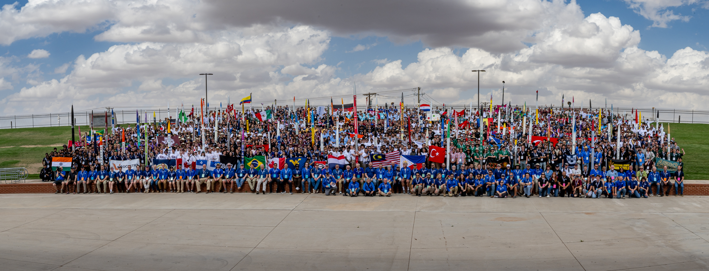 A very large group photo featuring hundreds of student teams. Some teams hold up their rocket while others proudly hold up flags from their home countries.