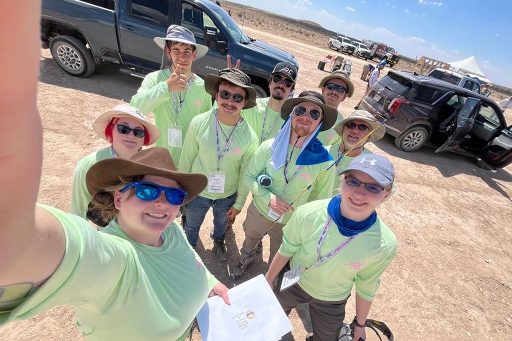 Nine people wearing light green shirts and hats stand for a group photo in the middle of the desert.