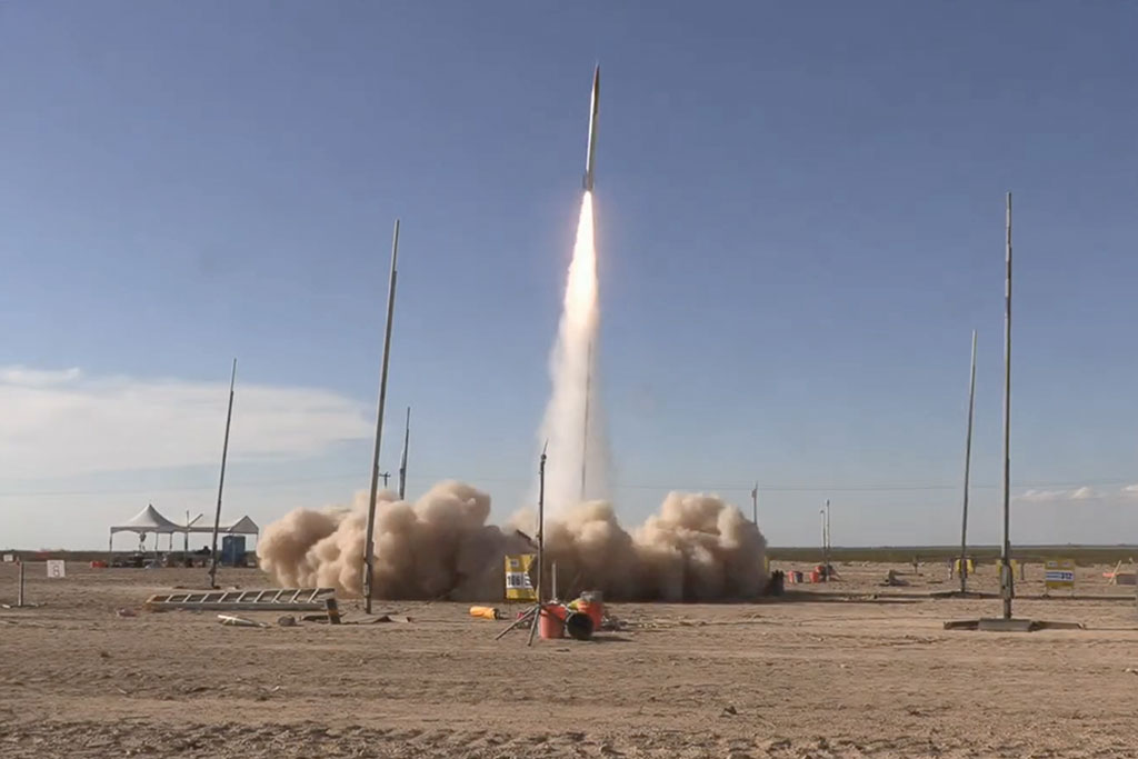 A rocket shoots up into the air, with a big cloud of dust forming below.