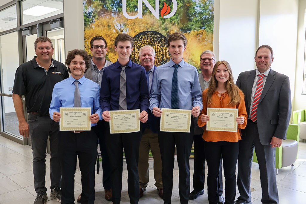 Four students smile and present certificates in a group photo. Five representatives from the Associated General Contractors of North Dakota stand behind them and smile as well.