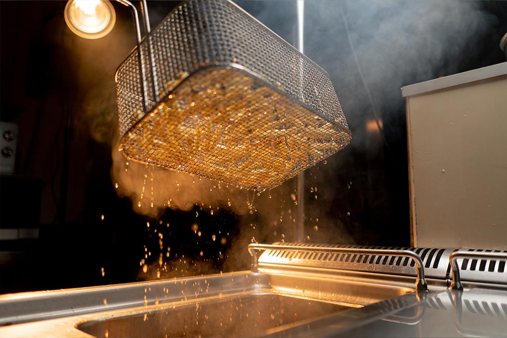 A close up of fries being cooked inside of a deep fryer basket.