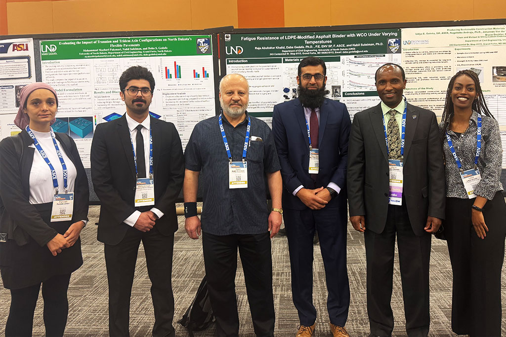 Six people stand for a group photo in front of research posters.