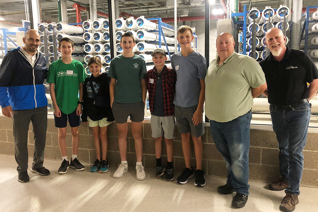 A group of faculty and middle school students smile for a group photo inside of the Grand Forks Water Treatment Plant.