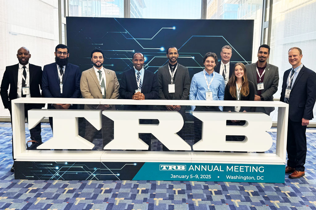 Eleven representatives from UND, including students and faculty, stand in front of a large photo opportunity booth that reads 'TRB' in large block letters.