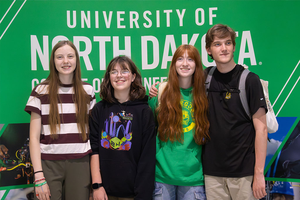 A group of happy high school students stand in front of a University of North Dakota backdrop.