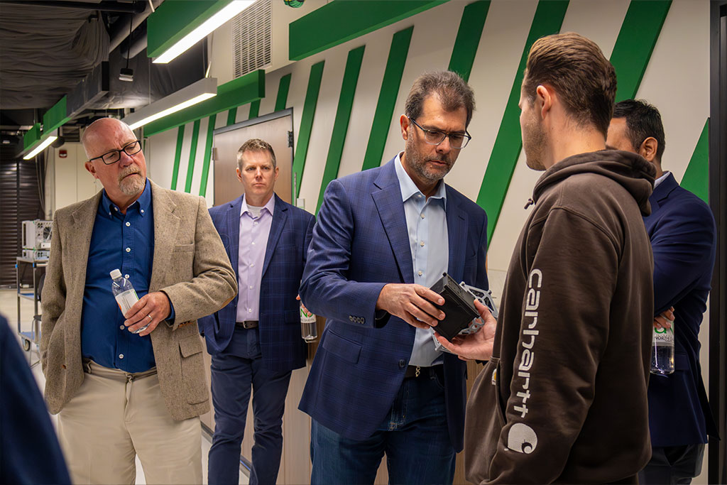 Men in business suits look at a prototype inside of the Mark & Claudia Thompson National Security Corridor at the University of North Dakota.
