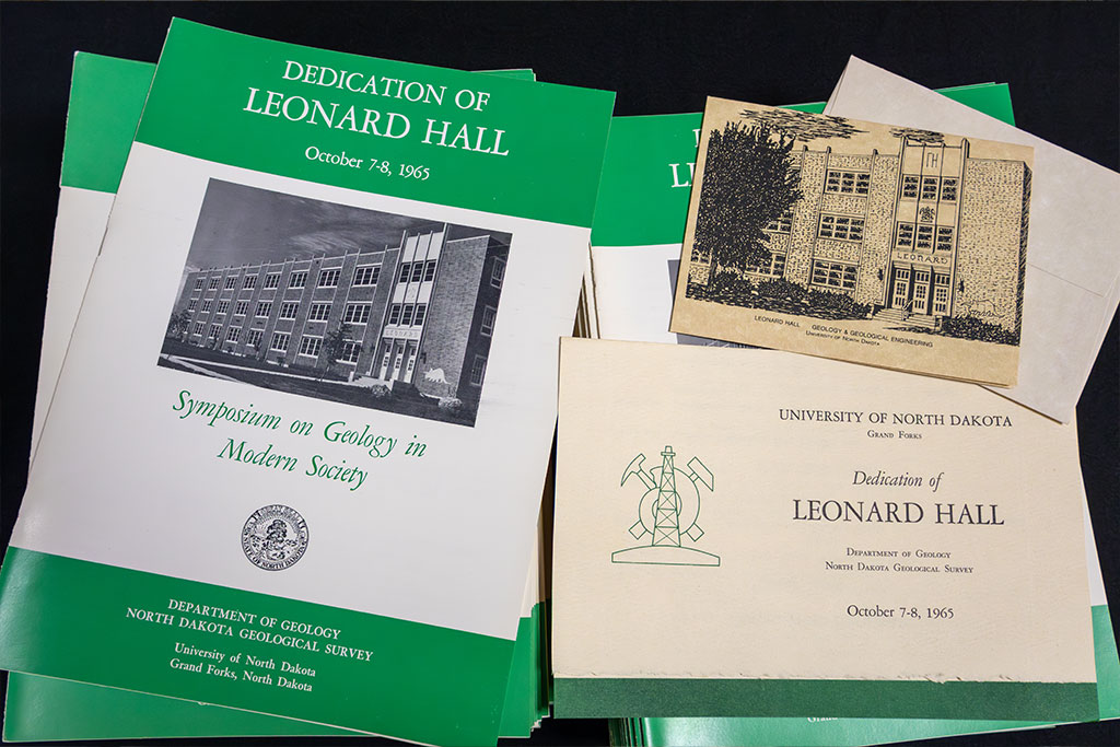 Archival print media displayed on a table, including event programs and invitations to Leonard Hall's dedication ceremony.