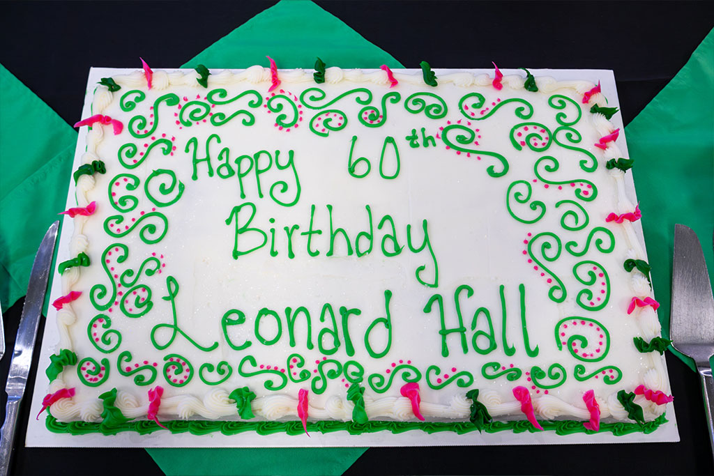 A white, green, and pink birthday cake with the following text written on it in icing: "Happy 60th Birthday Leonard Hall".