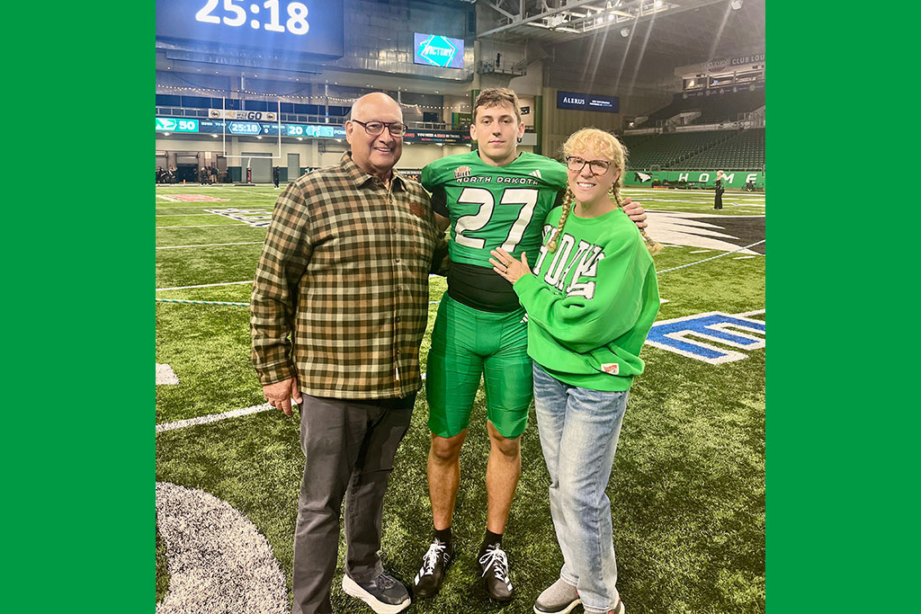 Two people stand next to a UND Fighting Hawks Football player inside of the Alerus Center.