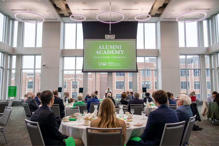 A person speaks at a podium inside of a brightly lit ballroom decorated in UND green.
