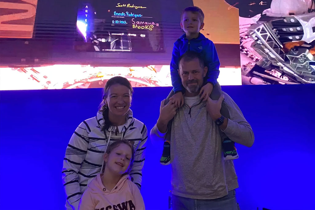 A family stands together in front of a digital display.
