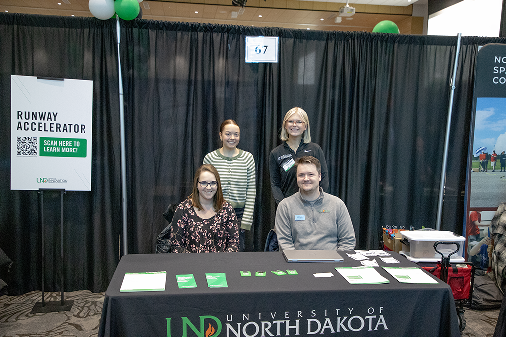 Four people stand at a booth for the University of North Dakota Runway Accelerator.