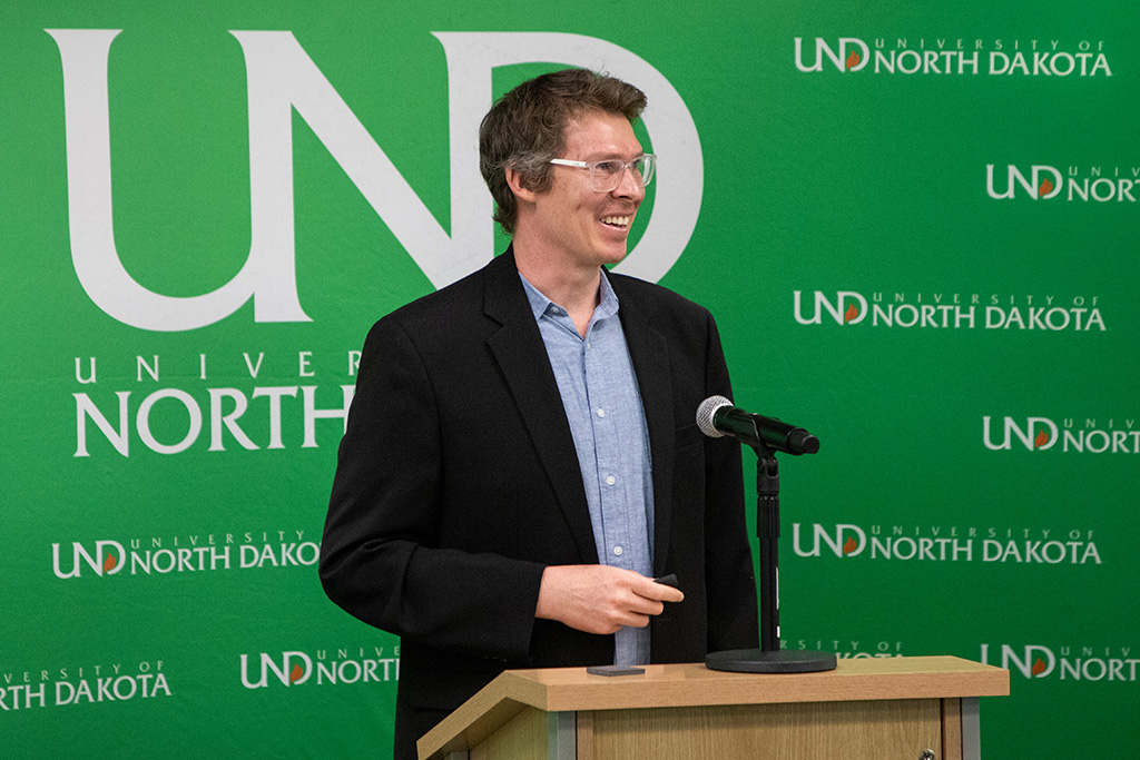 A person smiles as they speak in front of a University of North Dakota backdrop.