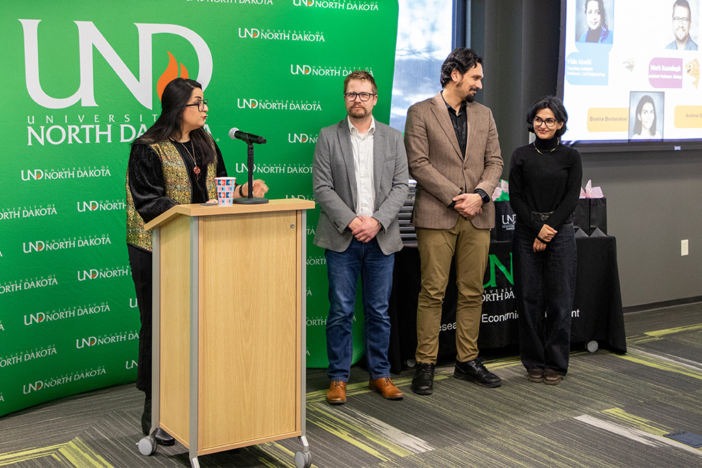 Faculty, staff, and a graduate student stand at a podium as they present to a room full of people.