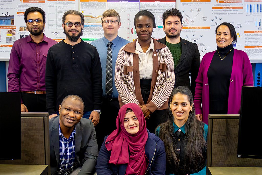Eight University of North Dakota students pose for a photo with Chester Fritz Distinguished professor Naima Kaabouch inside of the Artificial Intelligence Research Center.