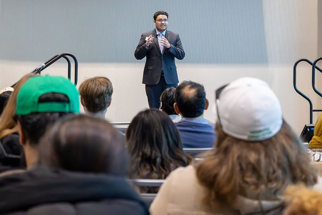 A student stands on a stage in front of an audience of people located in the University of North Dakota Memorial Union ballroom.