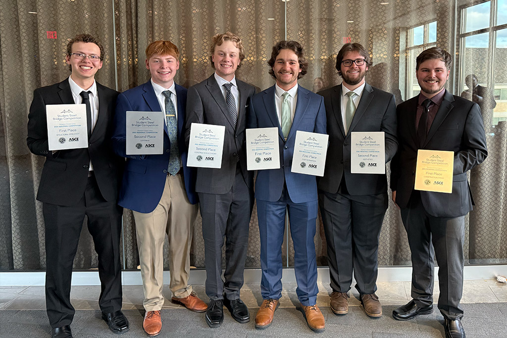 A group of college students hold first and second place award plaques for a group photo.