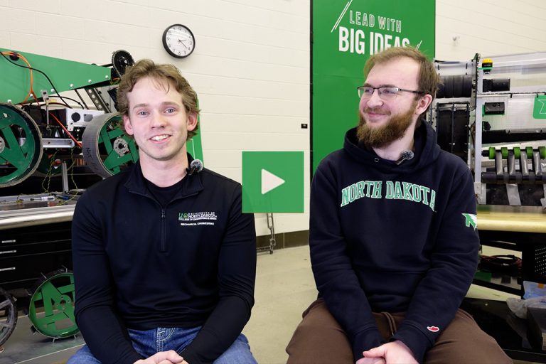 A video thumbnail of two University of North Dakota students smiling as they talk in a collaborative engineering high-bay lab.
