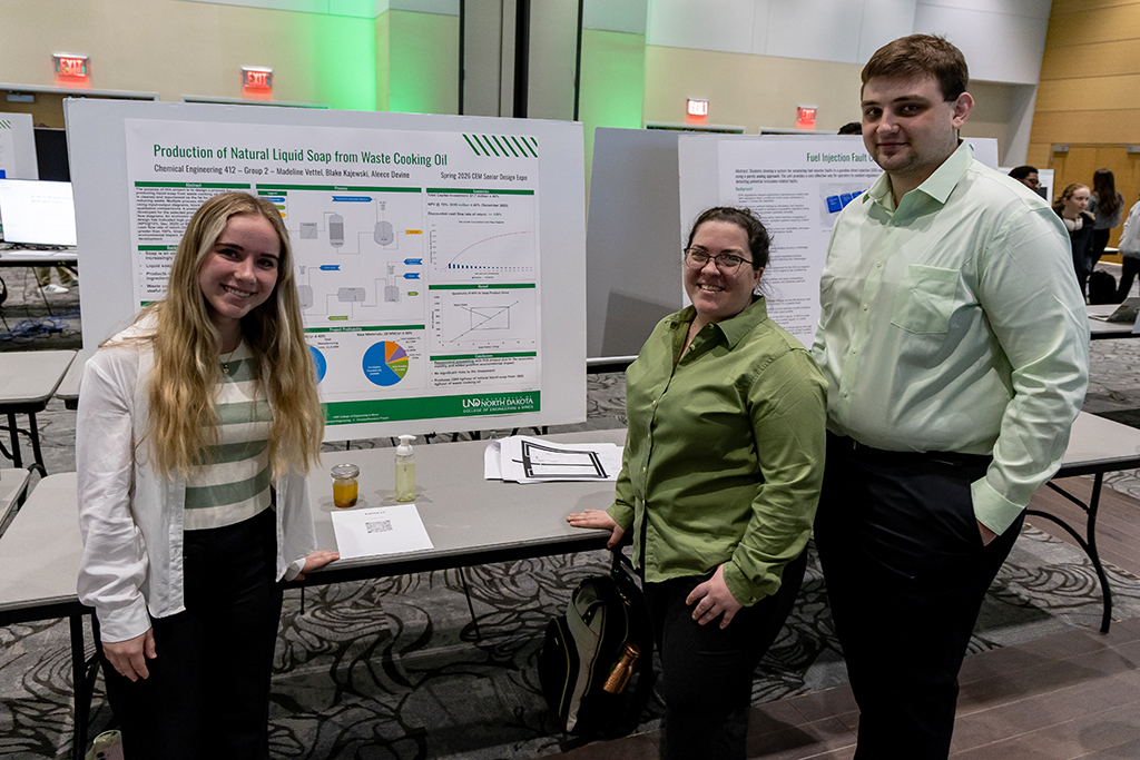 A group of students smile as they stand in front of their research design poster.